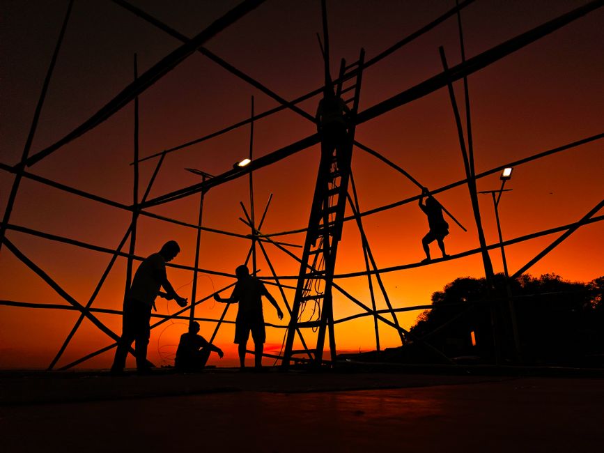 Silhouetted workers constructing bamboo scaffold at stunning sunset